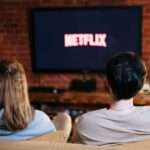 para siedząca na kanapie przed telewizorem, na którego ekranie wyświetla się napisz "Netflix"