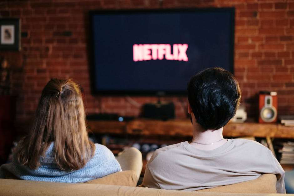 para siedząca na kanapie przed telewizorem, na którego ekranie wyświetla się napisz "Netflix"