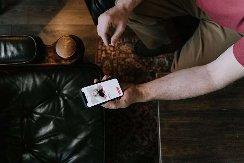 Mężczyzna trzymający smartfon z profilem randkowym podczas siedzenia w fotelu.