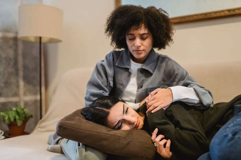 Kobieta z afro siedzi na kanapie, trzymając głowę drugiej kobiety na kolanach.