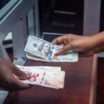 Dłonie przekazują sobie plik banknotów dolarów amerykańskich oraz waluty lokalnej w kantorze.