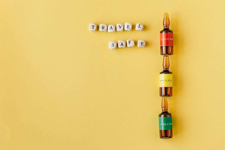 Trzy szklane ampułki z etykietami „VACCINE” obok drewnianych klocków z napisem „TRAVEL SAFE”.