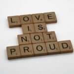 Drewniane płytki do gry w Scrabble układające się w napis LOVE IS NOT PROUD.