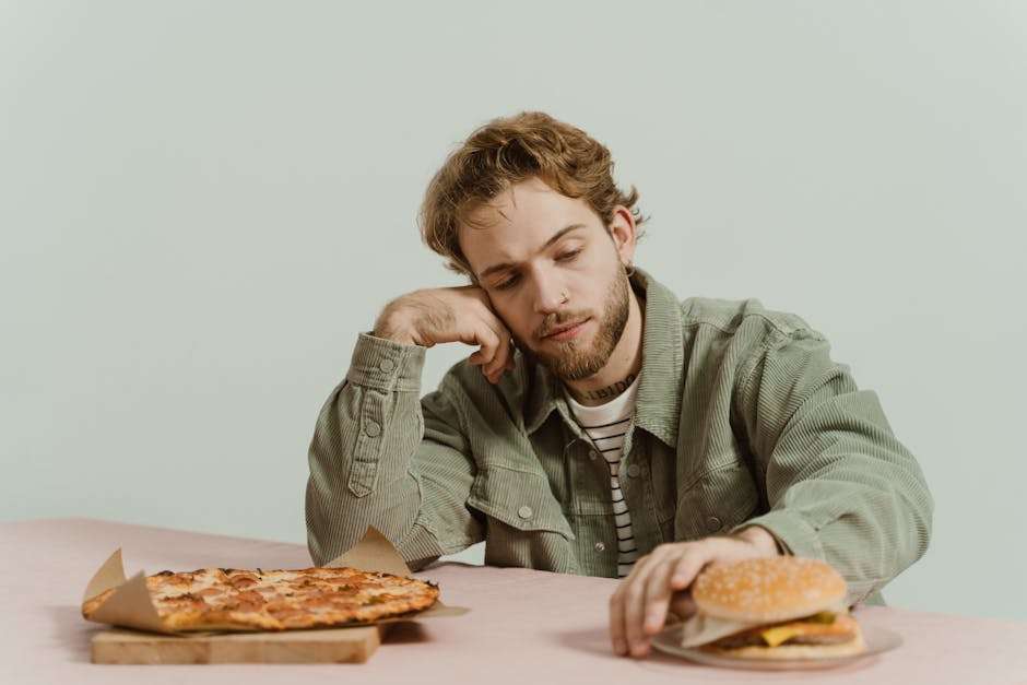 Mężczyzna siedzący przy stole z pizzą oraz burgerem na talerzu.