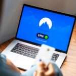 Osoba trzymająca kartę płatniczą przed laptopem z włączonym oprogramowaniem VPN.