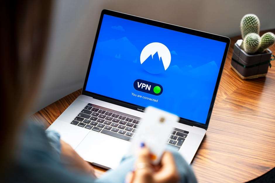 Osoba trzymająca kartę płatniczą przed laptopem z włączonym oprogramowaniem VPN.