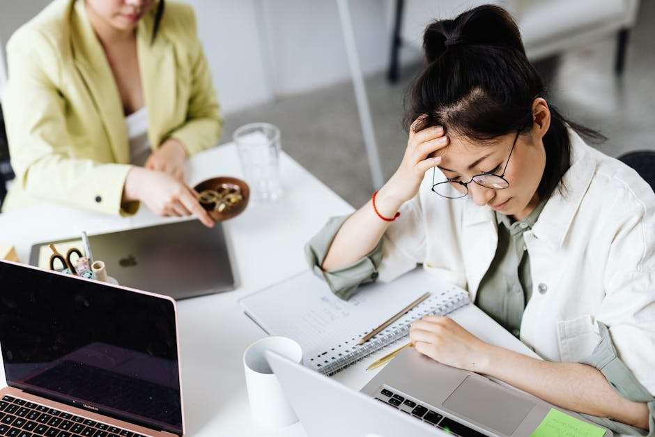 Dwie kobiety pracują przy laptopach na białym biurku w biurze.